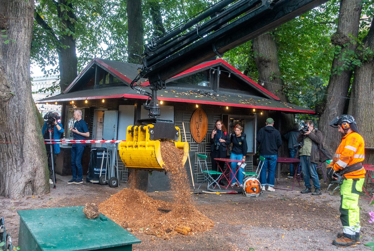 Grue hydraulique avec godet preneur jaune déchargeant des copeaux de bois dans un parc